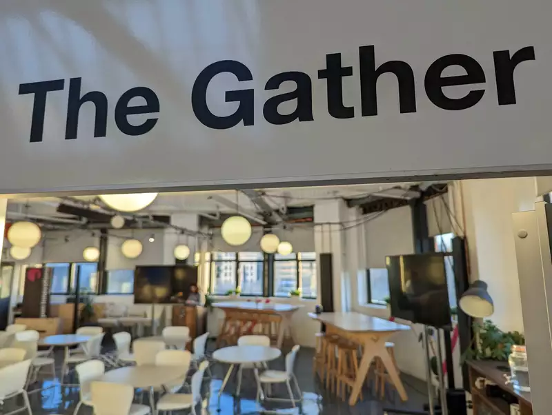 A view of The Gather. A large bright room with tables, chairs, and large TVs.